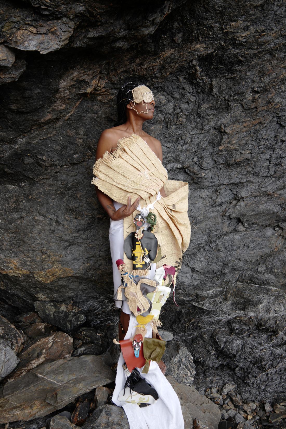 Même pose, cadrage légèrement différent : la femme tourne la tête de profil ; la colonne de poupées descend jusqu'aux rochers à ses pieds.