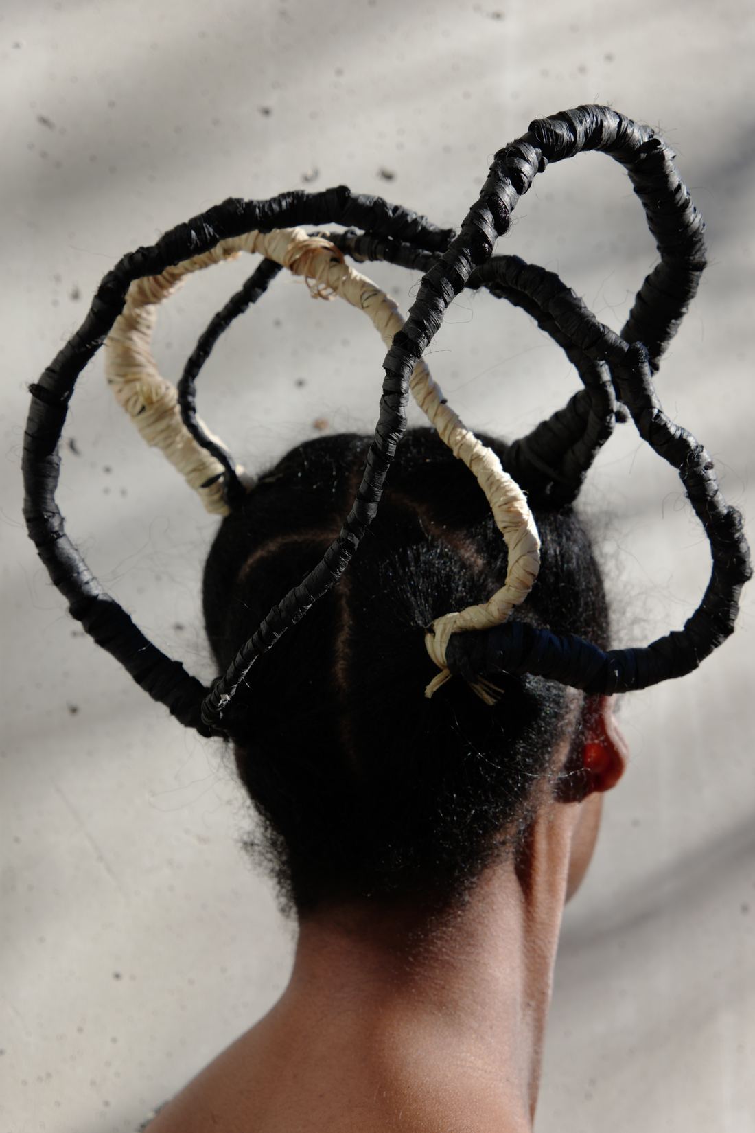 Plan vertical de dos, plus serré : les boucles noires et écrues s'élèvent au-dessus de la tête.