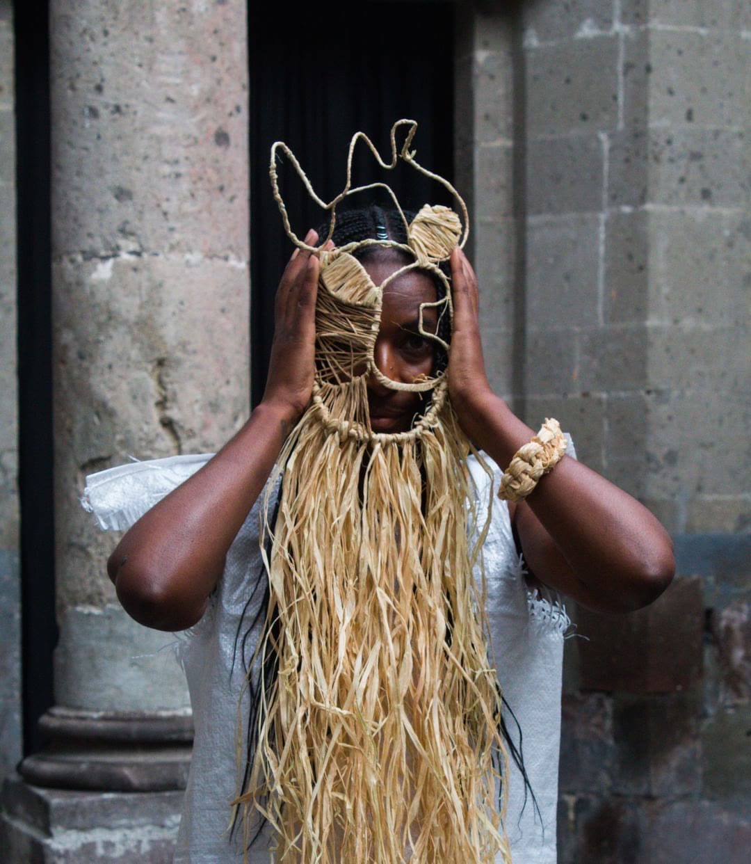 Daja au Centro de la Imagen à Mexico, les mains de chaque côté d’un masque prolongé de longues fibres de raphia.